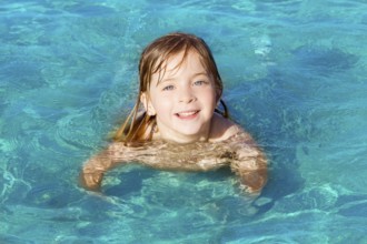Blond little girl swimming on turquoise beach in Ibiza
