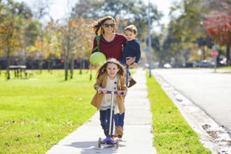 Mother daughter and son family in the park walking with ball and skate scooter