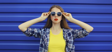 Portrait of modern stylish young woman in white glasses, casual clothing posing on blue wall