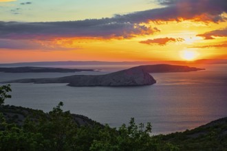 A calm sunset over the sea with an island in the foreground and colourful clouds in the sky,