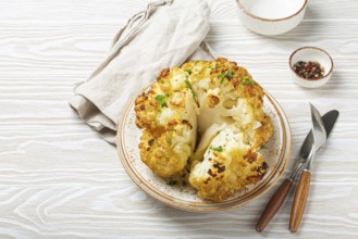 Whole roasted head of cauliflower with olive oil on plate on white wooden rustic table top view