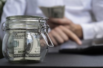 Dollar Banknote Saving Money In Glass Jar. Unrecognizable man calculate money on calculator