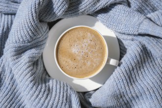 White cup of morning coffee on blue sweater background. Cozy home autumn concept. Aesthetics blog