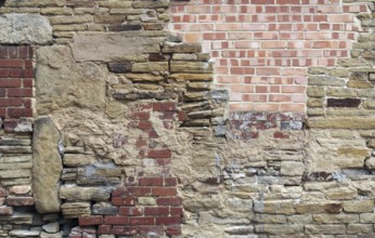 A large old wall made of mixed bricks and stone with many jumbled patched and uneven repairs
