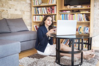Beautiful young woman, dressed elegantly, sits on the carpet in the coziness of her home, enjoying