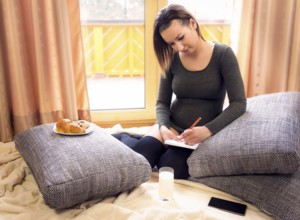Beautiful pregnant woman sits comfortable on pillows, in front of big windows, with snacks nearby