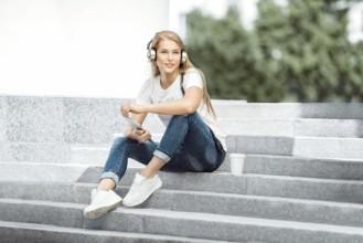 Happy young woman with vintage headphones and a cup of coffee to go, surfing the internet on a