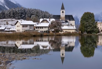 The church in the village Tarasp reflecting in the Taraspsee in the Swiss community Scuol in the