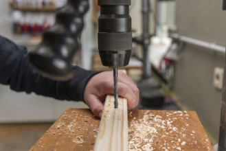Carpenter drills a hole in the wood with an electric drill - close-up