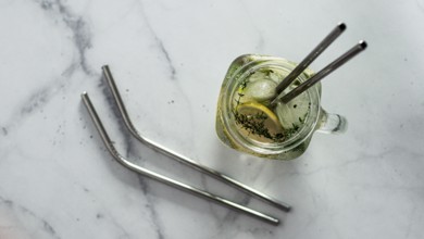 Metal drinking straws and cold drink in glass mason jar on white marble background. Top view or