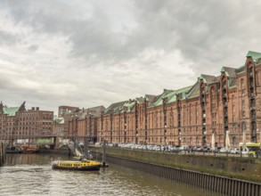 Yellow boat on a river next to historic brick-red buildings and a metal bridge under a cloudy sky,