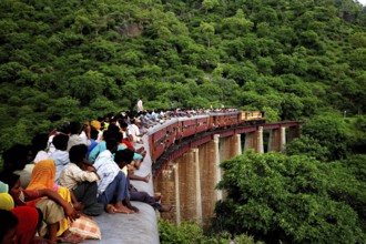 Commuters sitting on roof of train on bridge, Kamali Ghat, Rajasthan, India