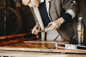Man applying varnish to wood with precision in a rustic workshop