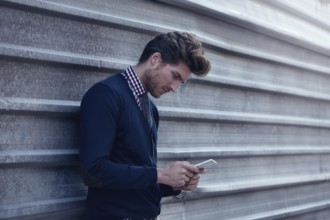 Young businessman texting smartphone phone on the street metal fence