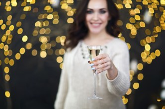 Smiling woman in the sweater with glass of champagne over lights background. Party, drinks,