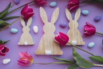 Easter eggs and wooden bunnies with pink tulips on violet pastel background. Flat lay composition,