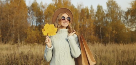 Autumn portrait of stylish happy young woman with shopping bag and maple yellow leaves, fashionable