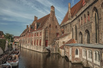 Old buildings on the canal bank, boats and sunny blue sky in Bruges. With many canals and old