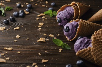 Wafer cones with blackberry icecream on wooden kitchen table with crumbs and berries aside