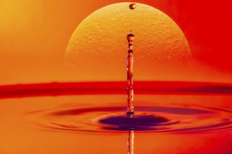 A single drop of water falling into a body of water with a glowing sunset in the background,