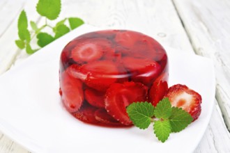 Strawberry jelly with mint and berries in a plate on a kitchen towel on the background light wooden