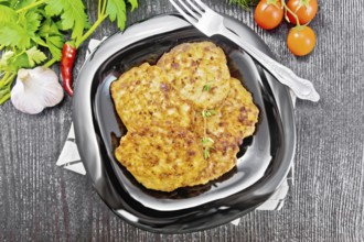 Fritters of minced meat in a plate with a fork on napkin, garlic, parsley and hot pepper on black