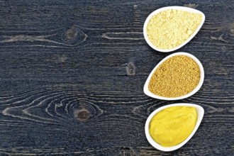 Mustard sauce, seeds and mustard powder in three saucepans on the background of a black wooden