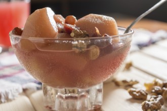 Apple compote with dried fruits in the cup on wooden table with decorative wallnuts
