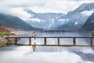 Woman sitting on a wooden bridge over the lake Hallstatter, admiring the peaks of the Austrian Alps