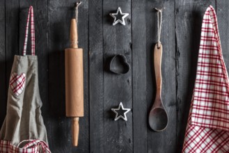Apron and other kitchen tools hanged with nails on a black wooden wall