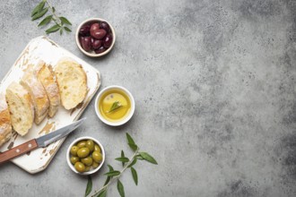 Sliced fresh ciabatta on cutting kitchen board, green and brown olives, olive oil with rosemary,