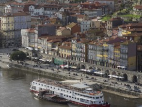 Colourful houses along a riverside street with boats in the river and lively street life, porto,