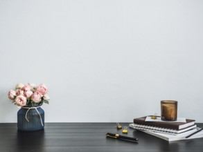 Home office desk with copy space. Pink flowers, scented candle, stack of books on black tabetop.