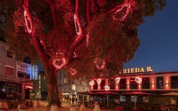 A tree with red heart-shaped lights decorates a lively urban scene at night, Hans-Albers-Platz, St.