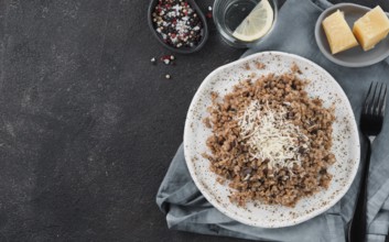 Buckwheat risotto with dried mushrooms served parmesan cheese in craft plate on black cement