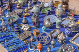 A colorful Moroccan market scene along a bustling street, with vendors selling spices, textiles,
