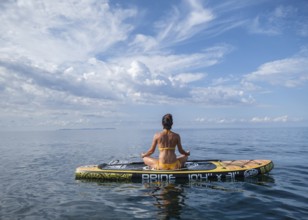Woman practicing yoga on a surfboard under a dramatic sky, Estalella, coast of Llucmajor, Majorca,
