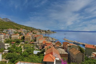 Coastal town with red roofs and views of the sea and distant mountains under a blue sky, Makarska