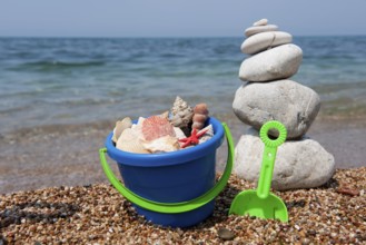 Shells on the beach in colorful bucket with stacked pebbles