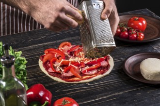 Cook in the kitchen putting the ingredients on the pizza on an old wooden background. Pizza concept