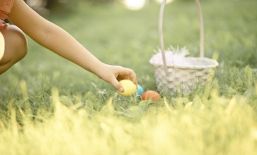 Little cute girl holding basket with colorful painted eggs on Easter egg hunt in park