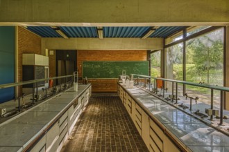 Empty classroom with view of green trees through windows, blackboard and laboratory tables,