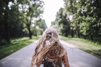 Girl with hair blown by wind running along a tree-lined road