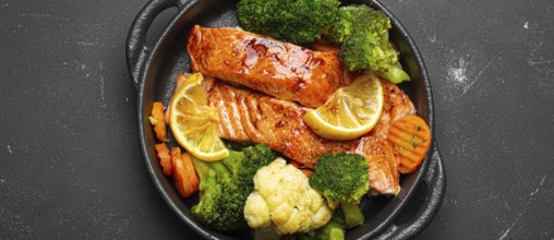 Healthy baked fish salmon steaks, broccoli, cauliflower, carrot in cast iron casserole bowl black