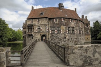 Wide bridge leads to a historic castle with moat, surrounded by nature, cloudy sky, lüdinghausen,