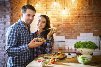Young smiling couple eating homemade pizza together at kitchen