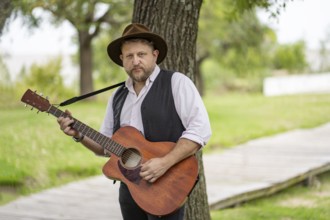 Musician posing for the camera while playing guitar in a park