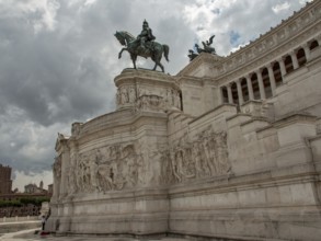 Large monument with equestrian statue and detailed sculptures in the background of clouds, Rome,