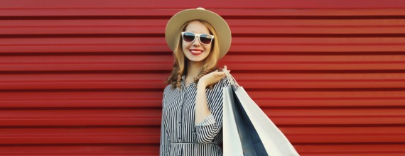 Stylish beautiful happy smiling young woman posing with shopping bags in summer straw hat on red