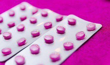 Pink pills in a blister on a pink background close up